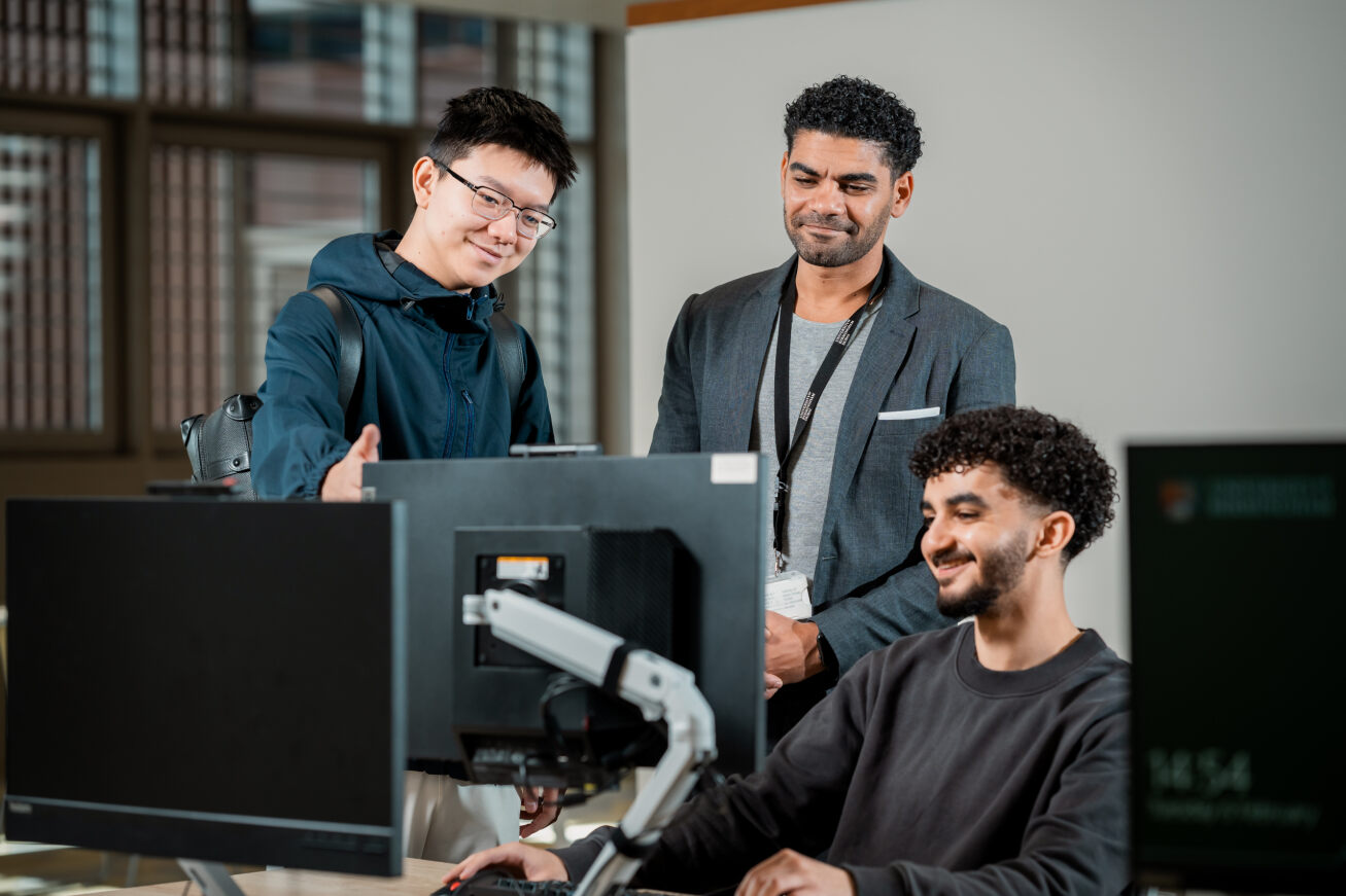 Two students and a staff member look at a computer screen